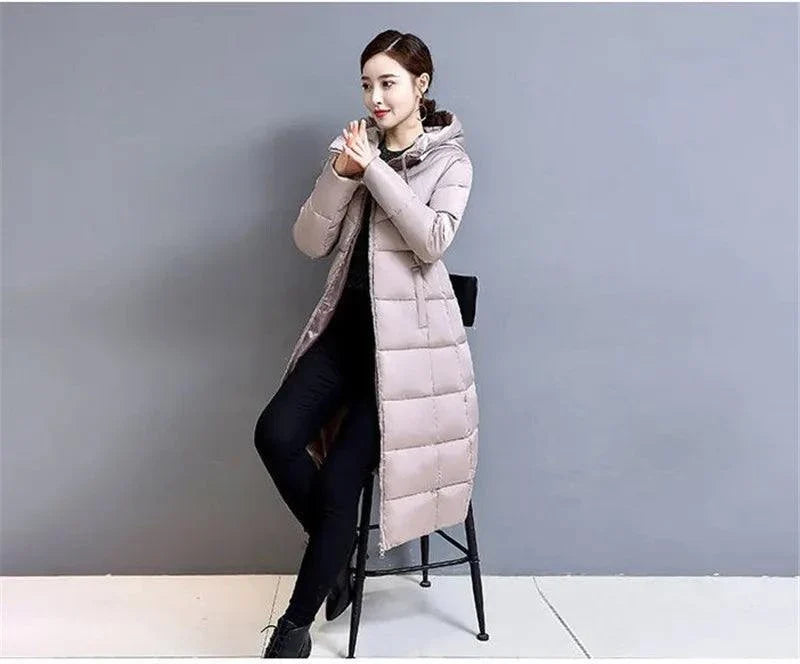 Woman wearing a long, slim-fit padded jacket with hood, seated, showcasing winter fashion.