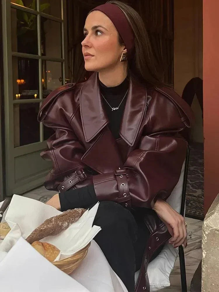 Vintage cropped leather jacket with braid lapel and zipper, worn by a woman seated in a cozy indoor setting.