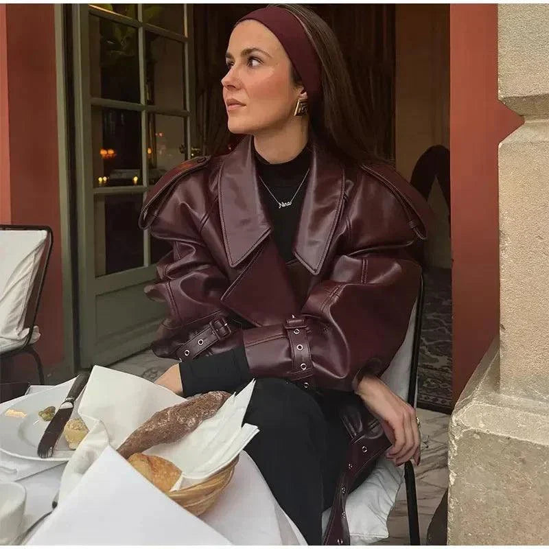 Vintage cropped leather jacket with braid lapel, long sleeves, and zipper closure in burgundy, modeled in a stylish outdoor setting.