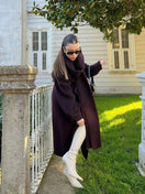 Switch Woman wearing an oversized red cape coat with a scarf collar in a stylish outdoor setting. 2 image